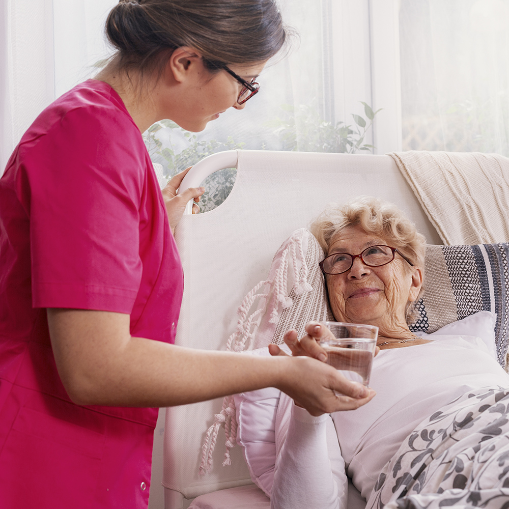 Beautiful young nurse serves tea to an elderly lady in a private Pleasanton Nursing Rehab